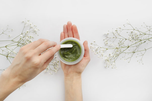 年轻女性双手使用绿色天然霜脸部或身体。有机天然护肤产品，花上白。洗剂或乳膏之包装。美容美容护肤理念。图片下载