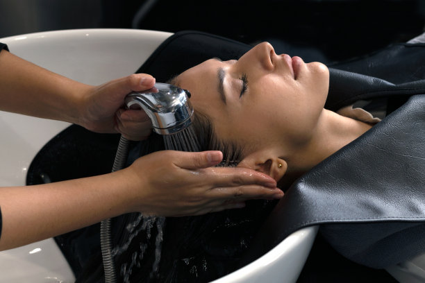 理发师在理发店里为顾客洗头，女人们躺在椅子上，穿着长袍，专业地照料头发和头皮。图片下载