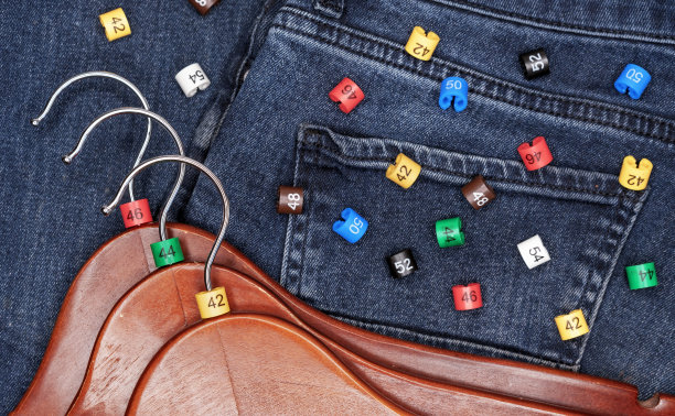 在牛仔布背景上有多种颜色的塑料尺寸标签的衣架。图片下载