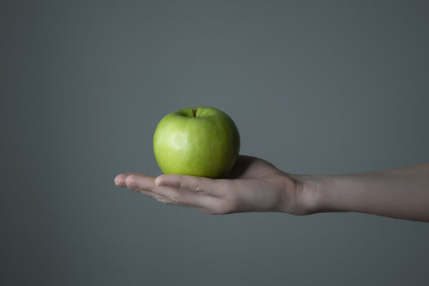 女人的手握青苹果灰色中性背景- raw照片。图片下载