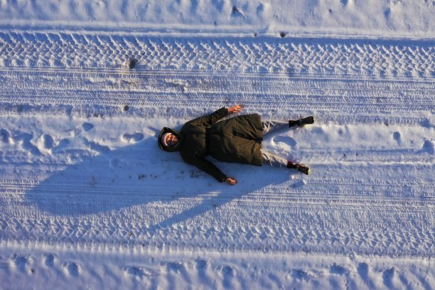 鸟瞰身穿绿色羽绒服的快乐女子躺在雪地上。阳光明媚的一天。冬天的心情。快乐的假期放松。寒冷的天气,霜图片下载
