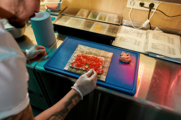 在商业厨房里，寿司师傅双手戴上防护手套，将红色鱼子酱涂在煮熟的米饭上，用虾做美味的卷饼图片下载