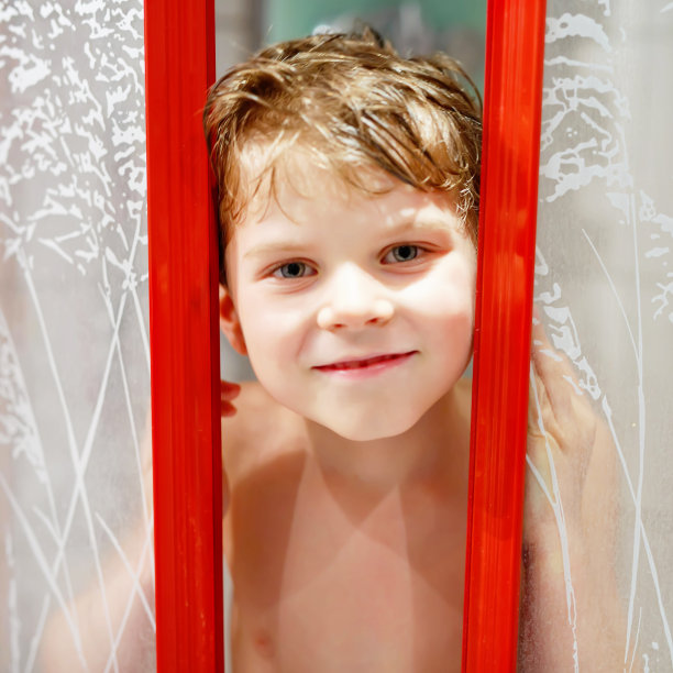 快乐的小男孩在淋浴间湿着，微笑着。素材图片