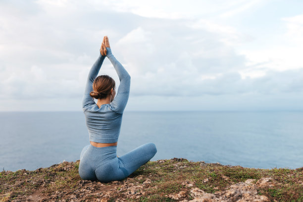 美丽的女人在悬崖上做瑜伽，在美丽的海景后面图片下载