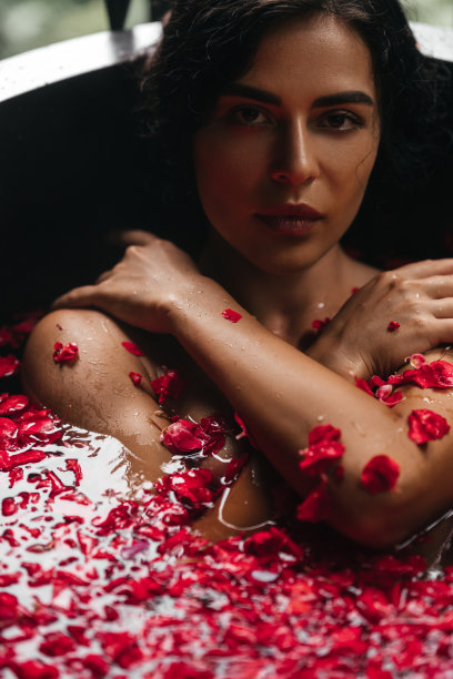 美女肖像，一个年轻女子的脸在浴池里，水里漂浮着红玫瑰花瓣和玫瑰花蕾。图片下载
