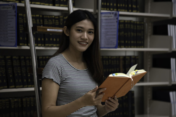 在图书馆里，亚洲学生在书架之间查找书籍。图片下载