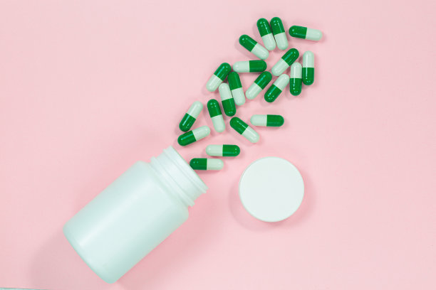 酸奶胶囊在一个玻璃瓶浅粉红色的背景与复制空间为您的文本。粉红色背景的白色益生菌胶囊。模板医疗博客社交媒体。图片下载