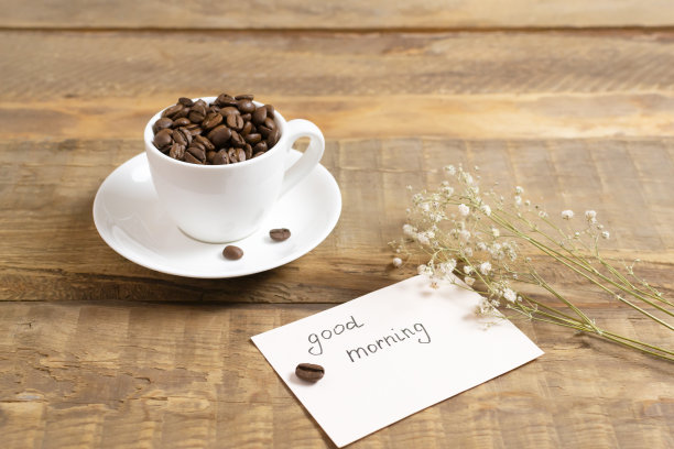 白色的杯子里装着咖啡豆，木质背景上有一张写着“早上好!”的卡片。图片下载