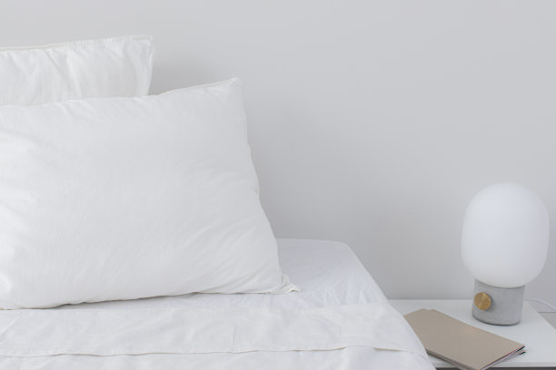 酒店房间里的床旁有蓬松的白色枕头和一盏灯图片下载