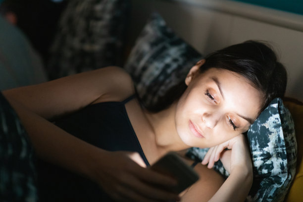 年轻女子盯着发光的智能手机屏幕，试图入睡图片下载