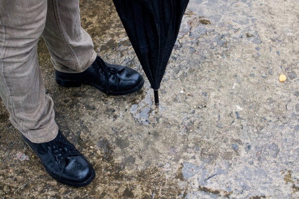 穿着靴子打着伞的男人在柏油路上图片下载