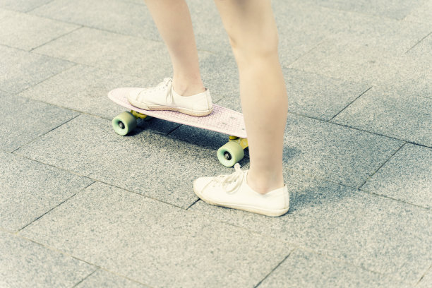 一个女孩的脚的近距离在白色运动鞋和粉红色便士滑板。图片下载