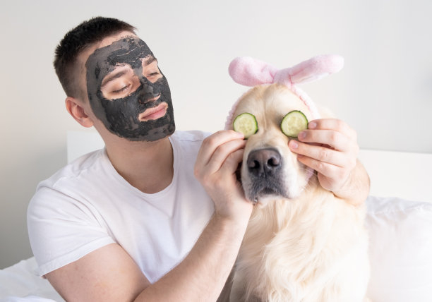 一个带着狗的男人在家照顾面部皮肤。一个家伙和一只金毛猎犬戴着一个粘土面膜。男性健康美容、美容、身体和皮肤护理的概念。图片下载