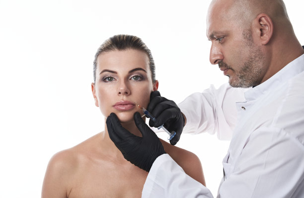英俊成熟的医生整形外科医生拿着一个注射器靠近一个美丽的女人的脸，使注射化妆品。图片下载