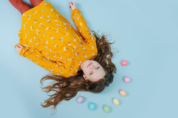 小女孩躺在地板上，她的头上有彩虹般的复活节彩蛋素材图片