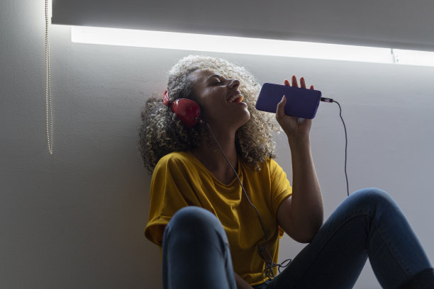 美丽的卷发黑发女人微笑着，喜欢听她的音乐耳机，她坐在窗前图片下载