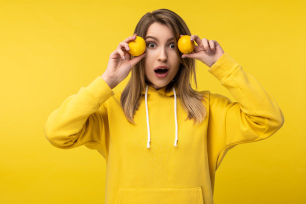 照片中迷人的女士摆出一种袜子的方式与柠檬。穿着休闲黄色连帽衫，孤立黄色背景图片下载