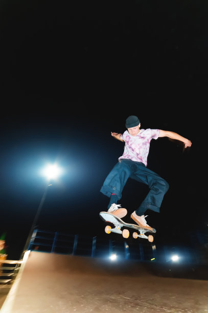 年轻的滑板者在一个晚上在滑板公园做一个跳跃戏法图片下载