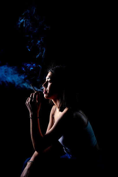 黑色背景上吸烟的年轻女子的肖像。香烟的概念。蓝色的烟雾。图片下载