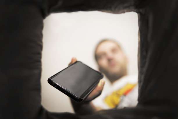 一名男子将无法工作的智能手机扔进垃圾桶。从垃圾桶俯视。垃圾回收和污染地球的问题。图片下载