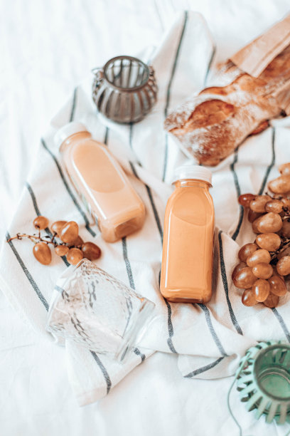 天然蔬菜汁装在塑料瓶里，葡萄和法式长棍面包放在毛巾上。野餐的概念。图片下载