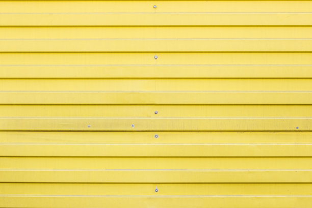 金属波纹型材的纹理与螺丝和铆钉。有水平线条的黄色墙壁。图片下载