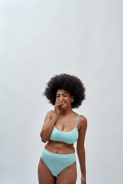 开朗的年轻非洲裔美国妇女与非洲式发型穿着蓝色内衣对着照相机笑，而摆出孤立的白色背景图片下载