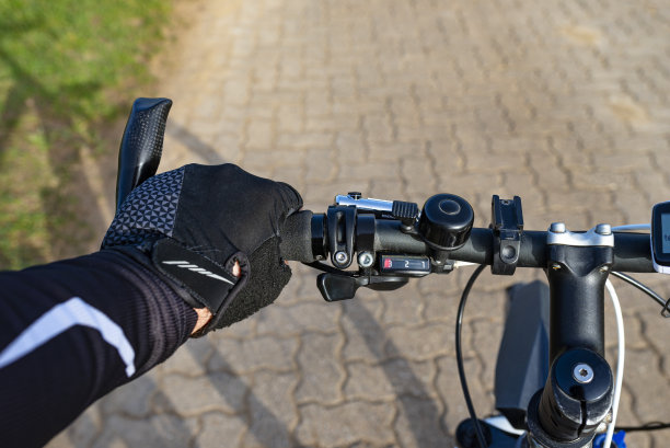 一种从第一人称角度看的自行车把手，一个男人的手放在把手上。可见自行车电脑和铃铛。图片下载