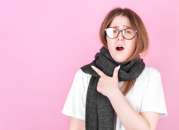 这张照片是在白色背景下拍摄的，一个戴着眼镜、裹着围巾的冷冰冰、沮丧的女孩用手指着空白的地方图片下载