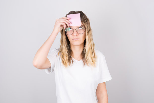 照片惊人的金发女人向上看与深刻思考的空白，与她的额头贴纸，孤立在灰色的背景图片下载