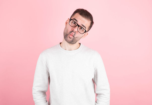 滑稽的喜剧演员在一天的学习后斗鸡眼，撅嘴，做鬼脸，做傻事。笨拙表情的笨男人在粉红色的背景下独自玩乐，装傻，孤立图片下载