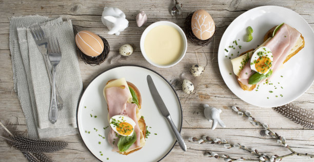 复活节早餐有金色的烤复活节条纹面包或黄油和奶酪的复活节面包，火腿鸡蛋，香葱和罗勒装饰在浅色的木制背景和美味的黄色酱汁图片下载