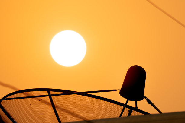 卫星技术碟式接收器在日出和金色的天空背景下，模糊的屋顶前景在阳光的光线图片下载