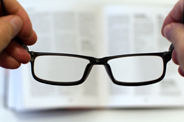 手拿眼镜在模糊的背景打开的书图片下载