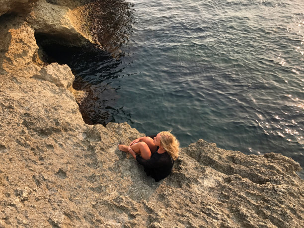 年轻漂亮的女人与金发坐在岩石海岸，夏天，浪漫的心情，悲伤，爱，反思，情绪，生活。图片下载