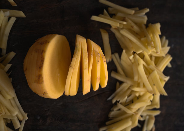 中间是圆形的切好的土豆，在自然光的照射下，在深棕色的木头背景上有一串切好的土豆。图片下载