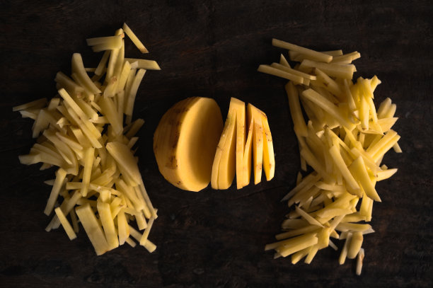 中间是圆形的切好的土豆，两边是一串切好的小土豆，在自然光下，暗棕色的木头作为背景。图片下载