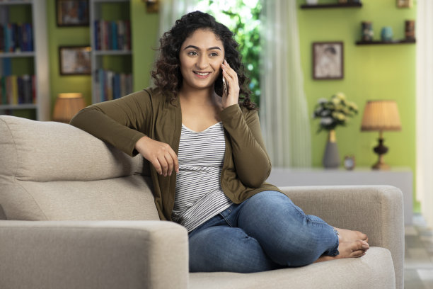 一个年轻女人坐在家里的沙发上打电话的照片:库存照片图片下载