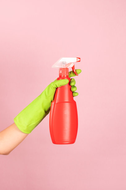 工人的手戴着绿色的保护手套，粉红色的背景上有一个红色的喷雾器。防止细菌、细菌和病毒。家用化学品广告图片下载