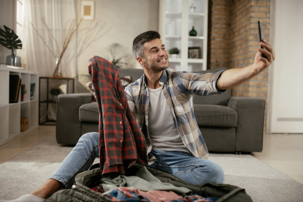 微笑的年轻人把衣服装进旅行袋。库存图片图片下载