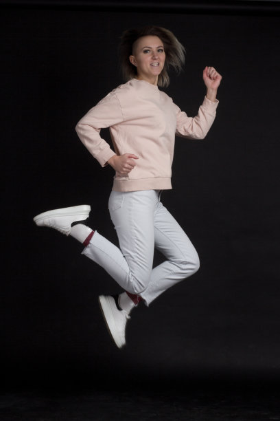 女人金发跳在黑色背景的浅粉色自行车，牛仔裤和皇冠，运动和健康的概念图片下载