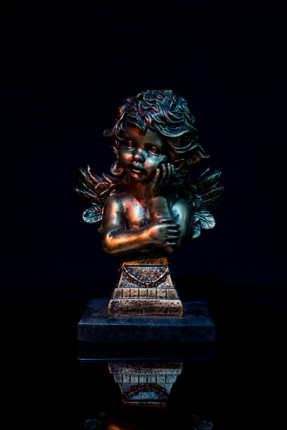 用树脂制成的天使雕像，上面覆盖着一个金色的浴缸，上面有一个古老的装饰，在黑色的背景上有反射图片下载