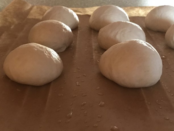 8个新鲜的白色面粉面包与油滴在棕色烘焙纸的特写图片下载