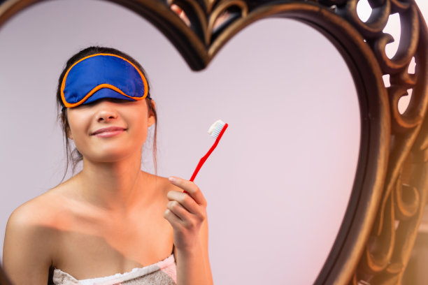 一个蒙着眼睛的黑发女人正在镜子前刷牙。晚上的程序。例程。牙科保健。图片下载