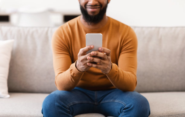 无法辨认的黑人在室内使用手机，裁剪，专注于手机图片下载