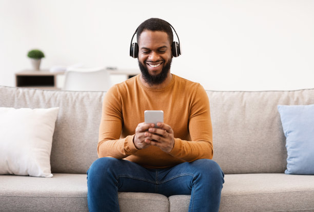 非洲男子戴着耳机在室内听手机音乐图片下载