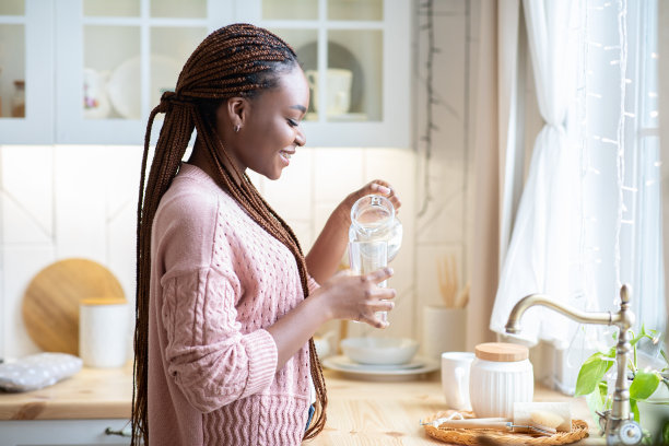年轻的非洲裔美国女士在厨房里把水从水壶里倒进杯子里图片下载