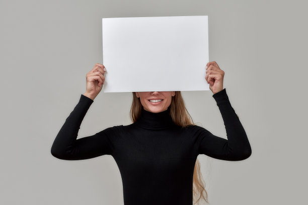 微笑的年轻白人妇女的肖像长头发穿着黑色高领举着白色空白旗帜在她的脸，孤立地站在灰色的背景图片下载