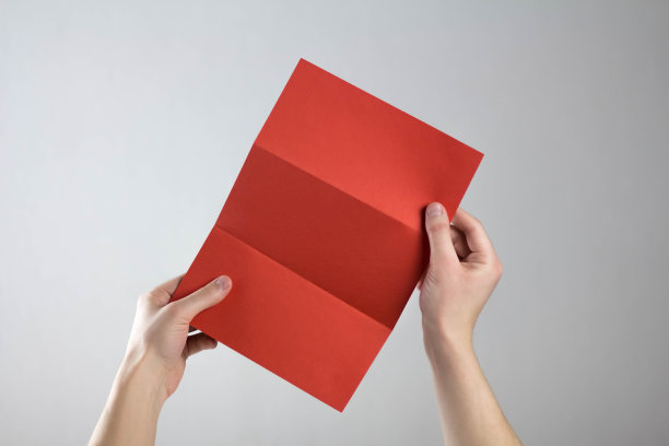 手上拿着一张红色的三折传单。一个干净的传单在你的手中。为你的文本。孤立在灰色背景上图片下载