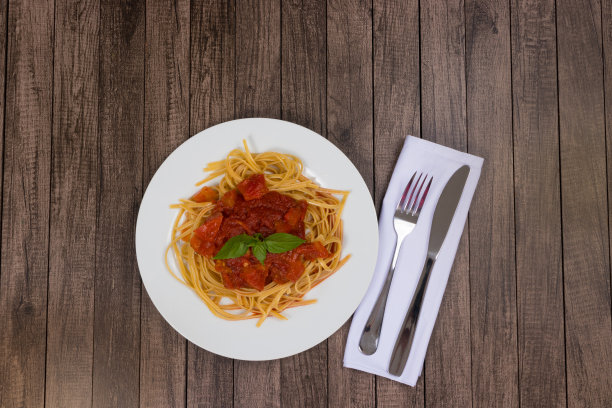 意大利面配番茄酱和罗勒叶。红酱香肠意面。顶部照片与顶部空间的文本。餐具在餐巾上。受欢迎的意大利面图片下载